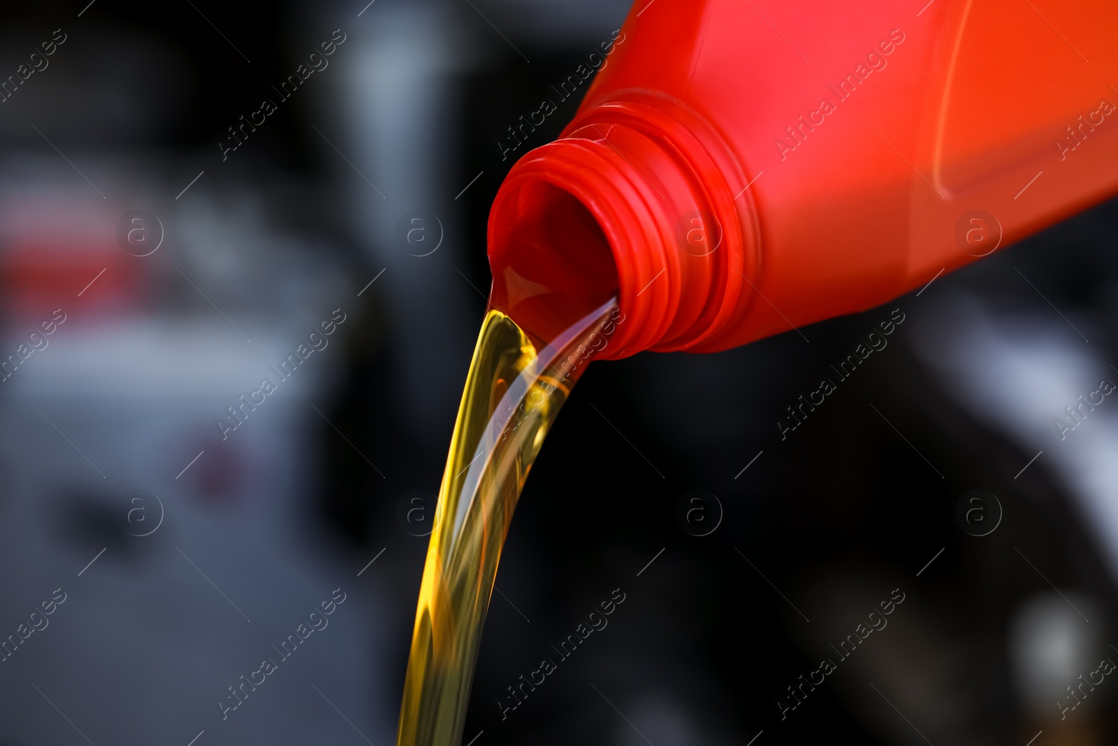 Photo of Pouring motor oil from red container against blurred background, closeup