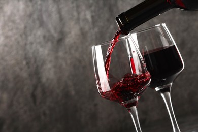 Pouring red wine into glass against grey background, closeup. Space for text