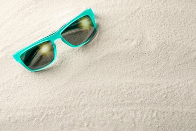 Stylish sunglasses on white sand, top view. Space for text