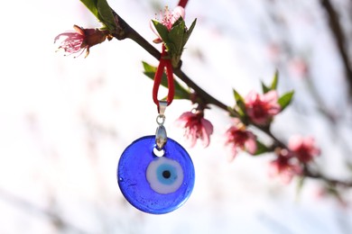 Photo of Evil eye amulet hanging on blossoming spring tree outdoors. Space for text