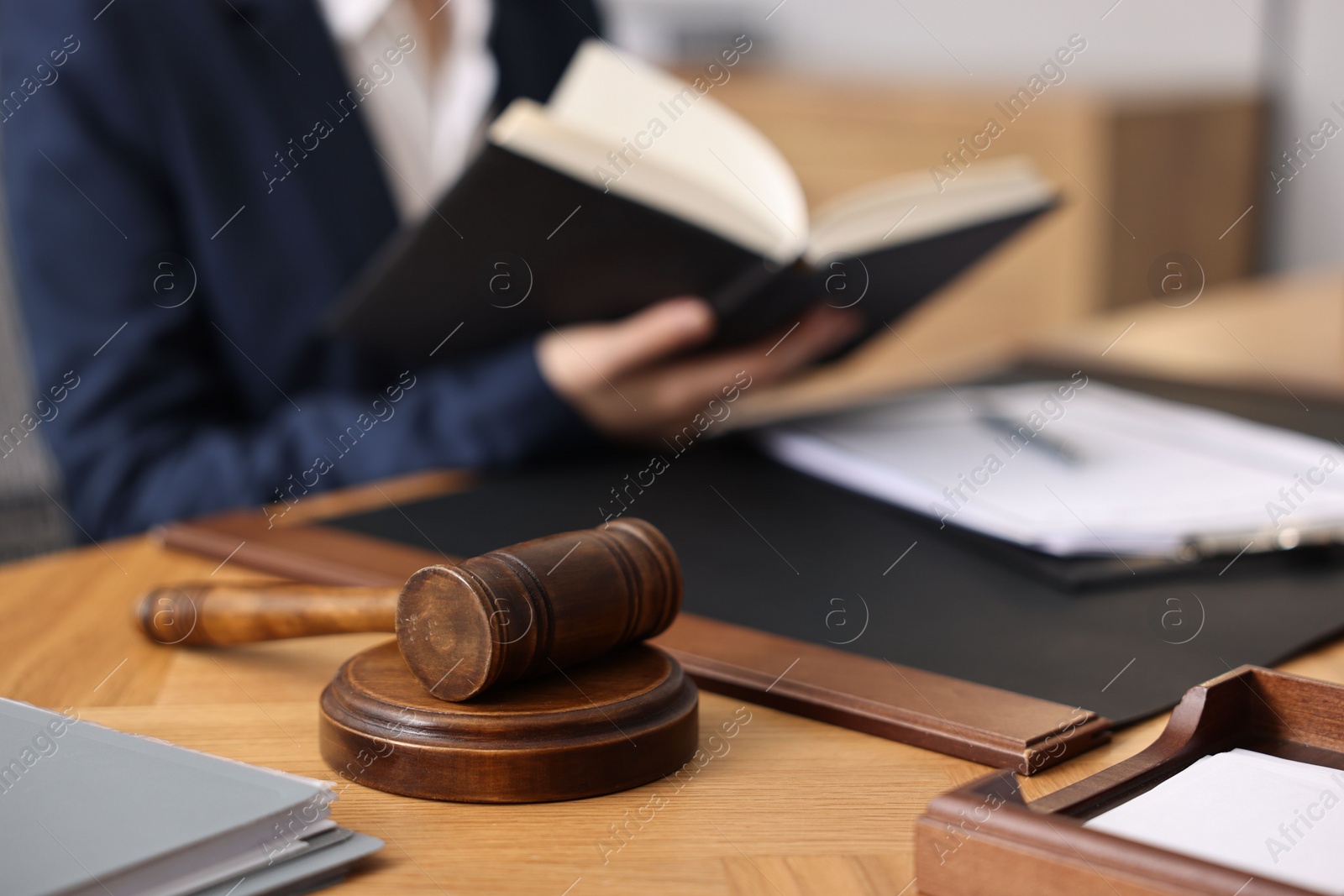 Photo of Notary reading book at wooden table in office, focus on gavel