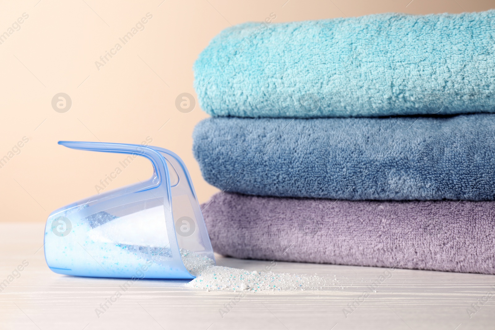 Photo of Measuring cup with washing powder and clean towels on table against color background. Laundry day