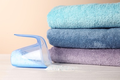 Measuring cup with washing powder and clean towels on table against color background. Laundry day