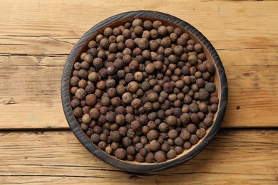 Aromatic allspice pepper grains in bowl on wooden table, top view