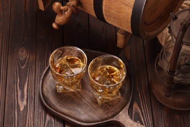 Whiskey with ice cubes in glasses and barrel on wooden table