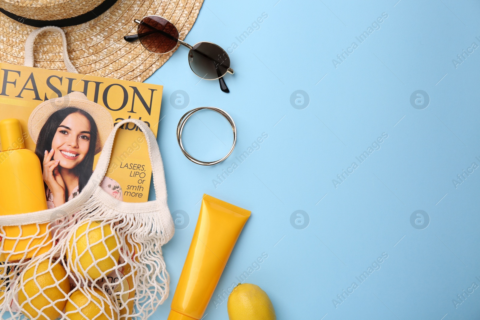 Photo of String bag with magazine, lemons and summer accessories on light blue background, flat lay. Space for text