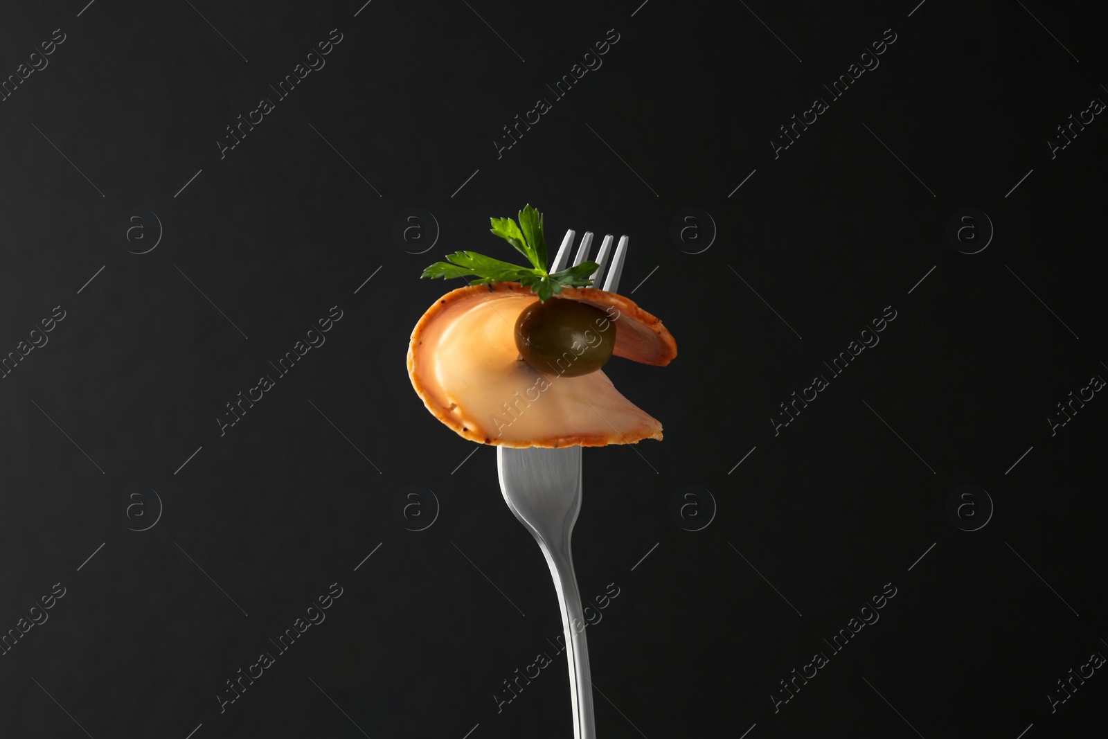 Photo of Fork with slice of ham, olive and parsley on black background