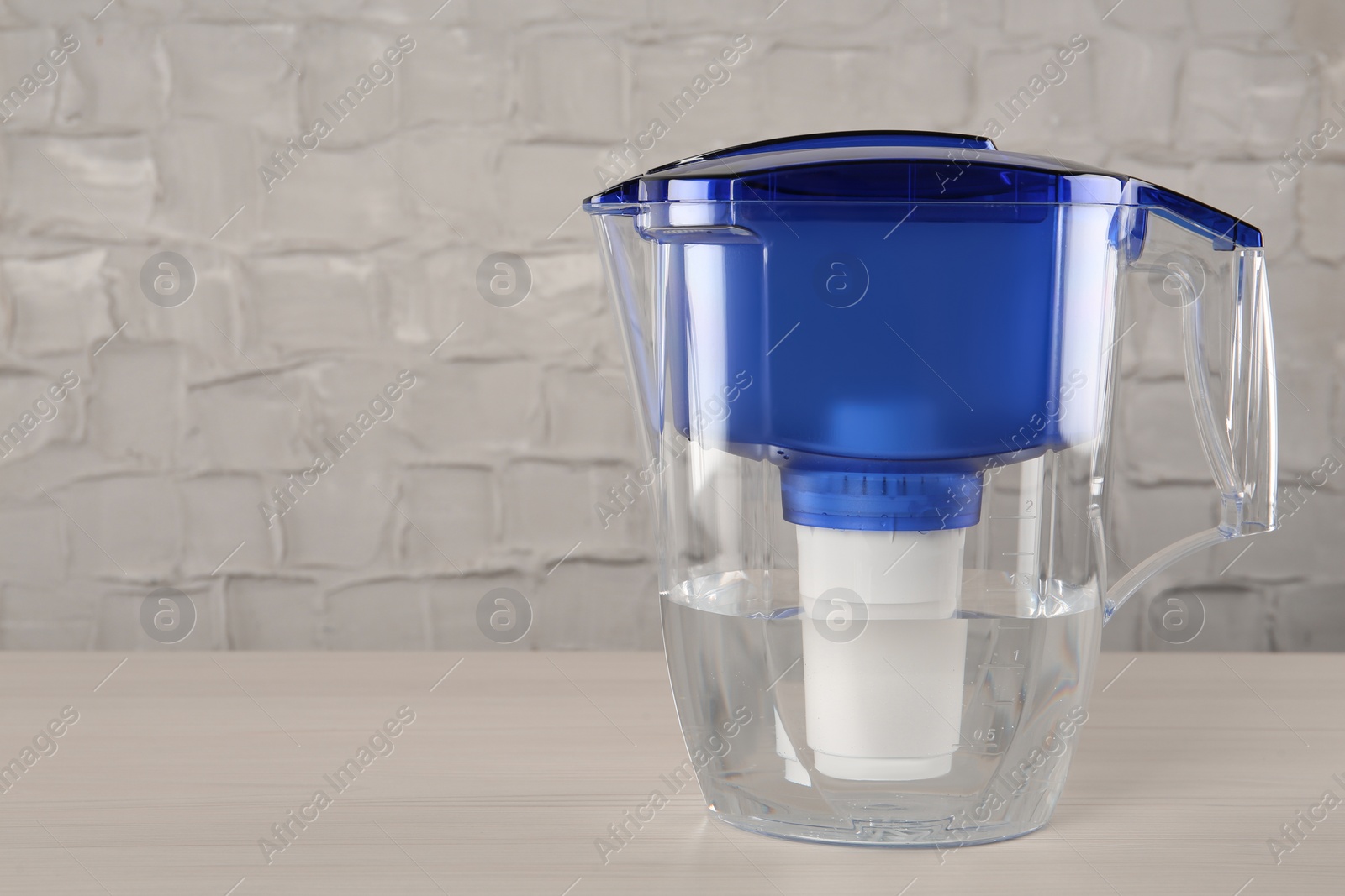 Photo of Filter jug with purified water on white table indoors. Space for text