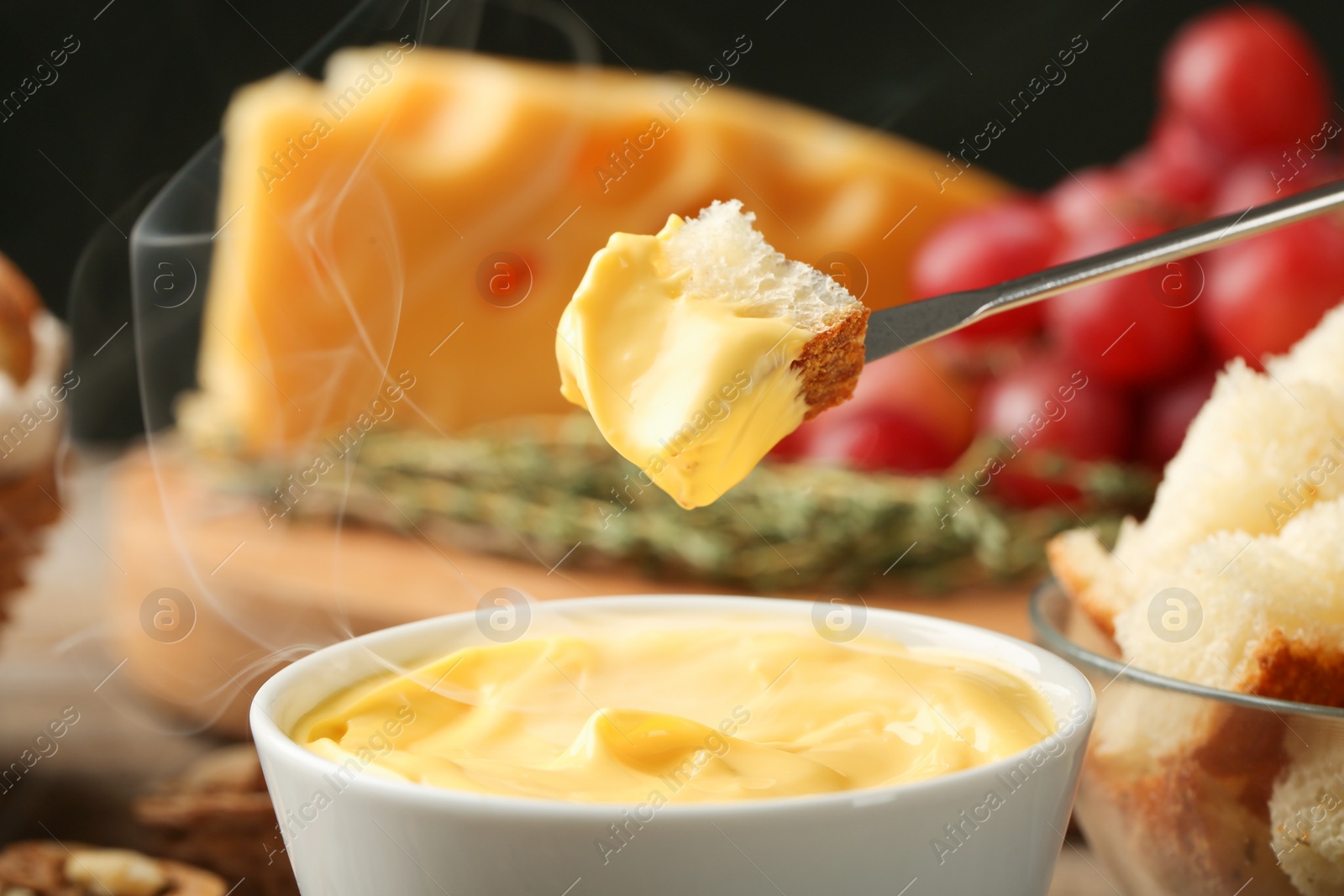 Photo of Piece of bread over bowl with delicious cheese fondue, closeup