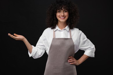 Happy woman wearing kitchen apron on black background. Mockup for design