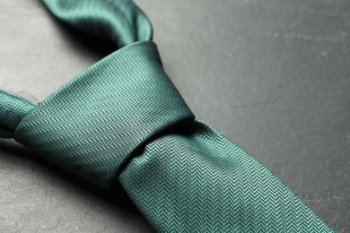 Photo of One green necktie on grey textured table, closeup