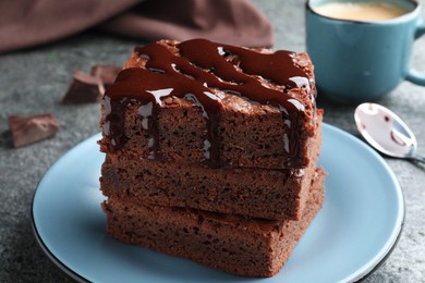 Delicious chocolate brownies with sweet syrup served on grey table, closeup