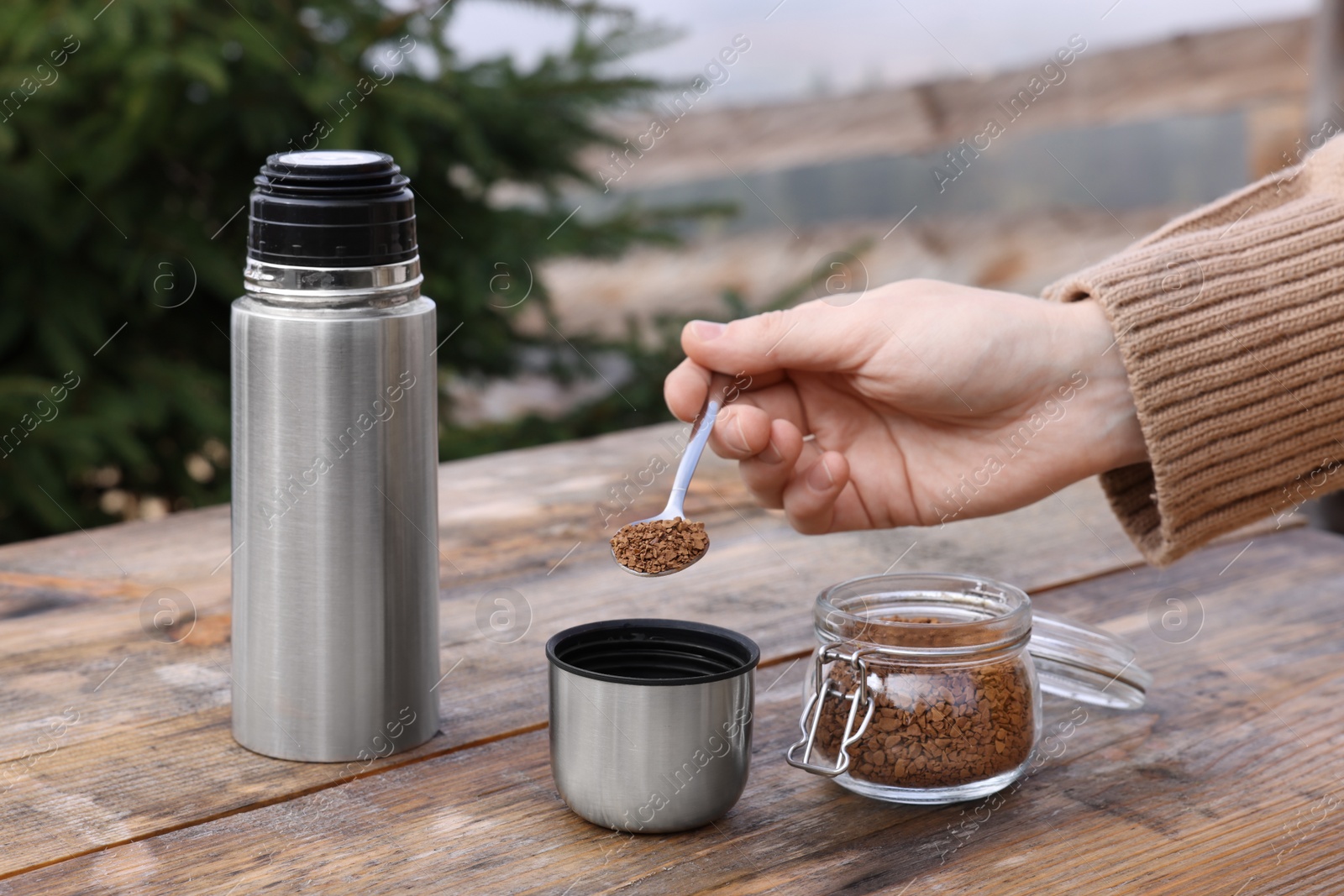 Photo of Woman making instant coffee at wooden table outdoors, closeup