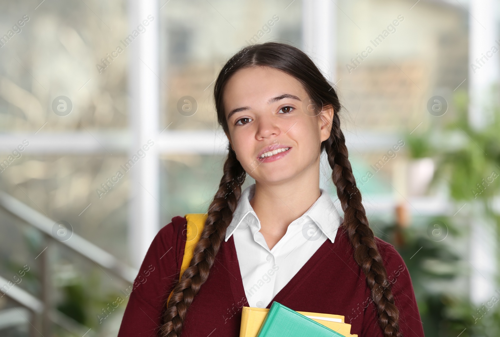 Photo of Teenage girl in school uniform with books and backpack indoors