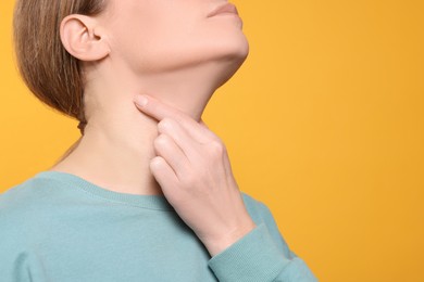 Woman suffering from sore throat on orange background, closeup. Space for text