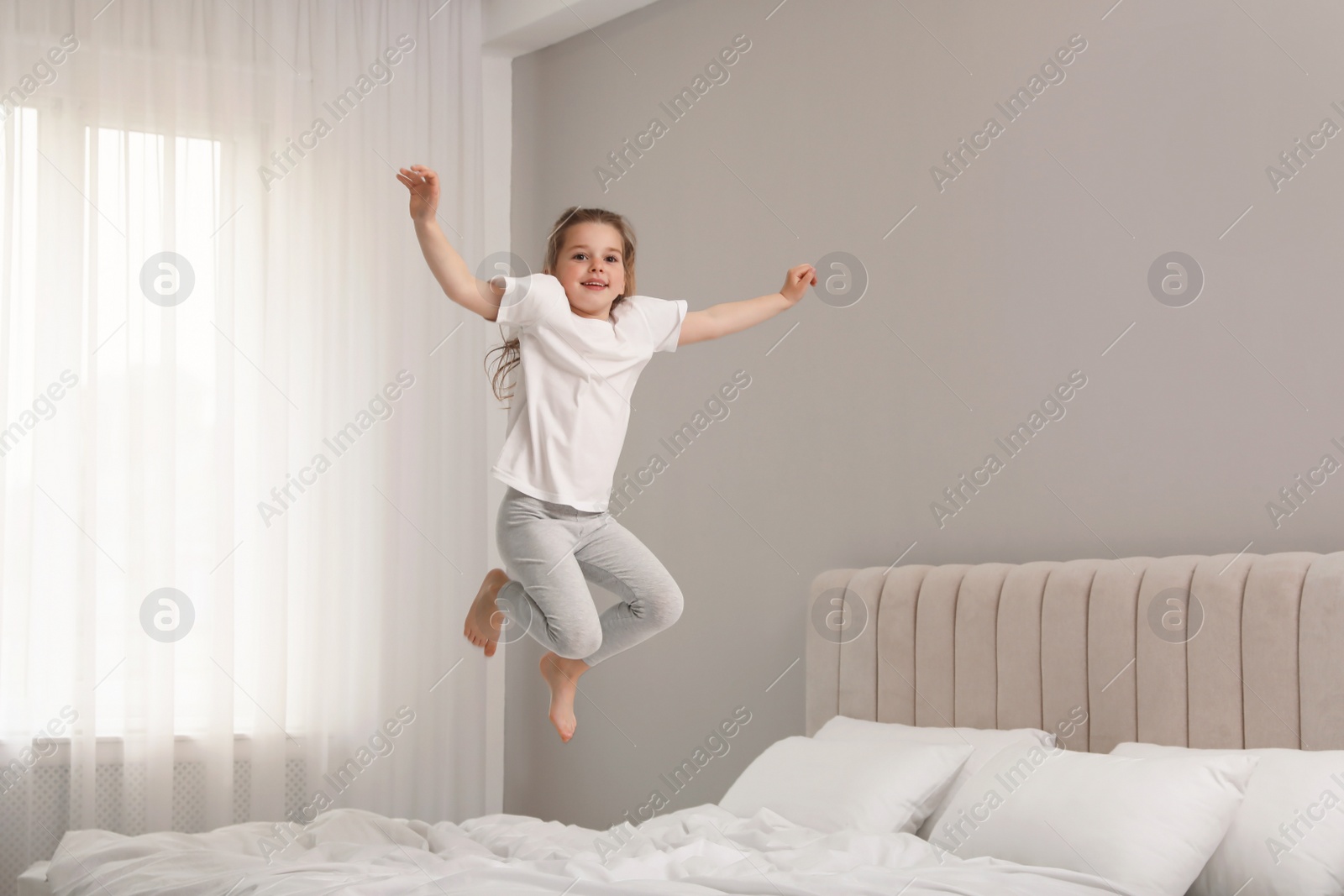 Photo of Cute little girl jumping on bed at home