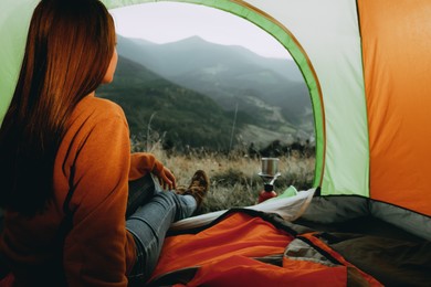 Photo of Young woman enjoying mountain landscape in camping tent, view from inside
