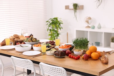 Healthy vegetarian food, glasses of juice, cutlery and plates on wooden table indoors