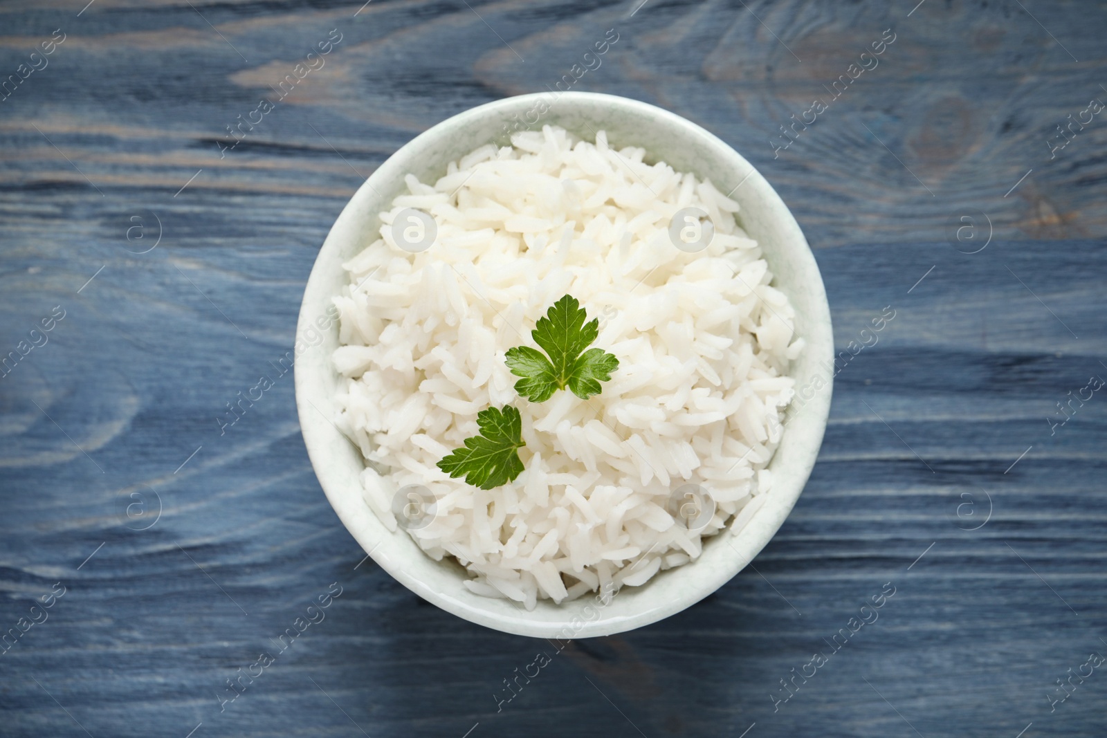 Photo of Bowl of tasty cooked rice with parsley on wooden background, top view