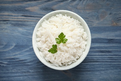 Photo of Bowl of tasty cooked rice with parsley on wooden background, top view