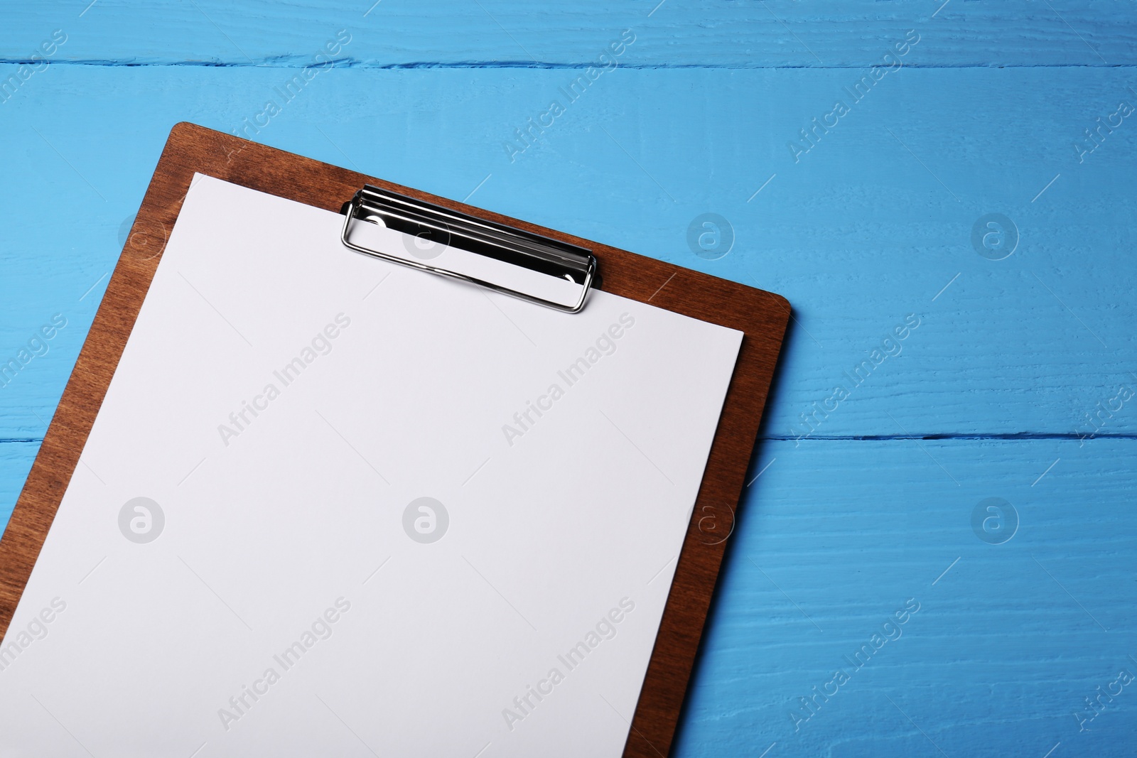 Photo of Clipboard with sheet of paper on light blue wooden table, top view. Space for text