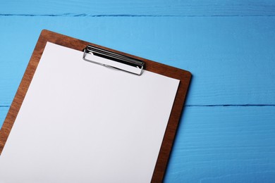 Photo of Clipboard with sheet of paper on light blue wooden table, top view. Space for text