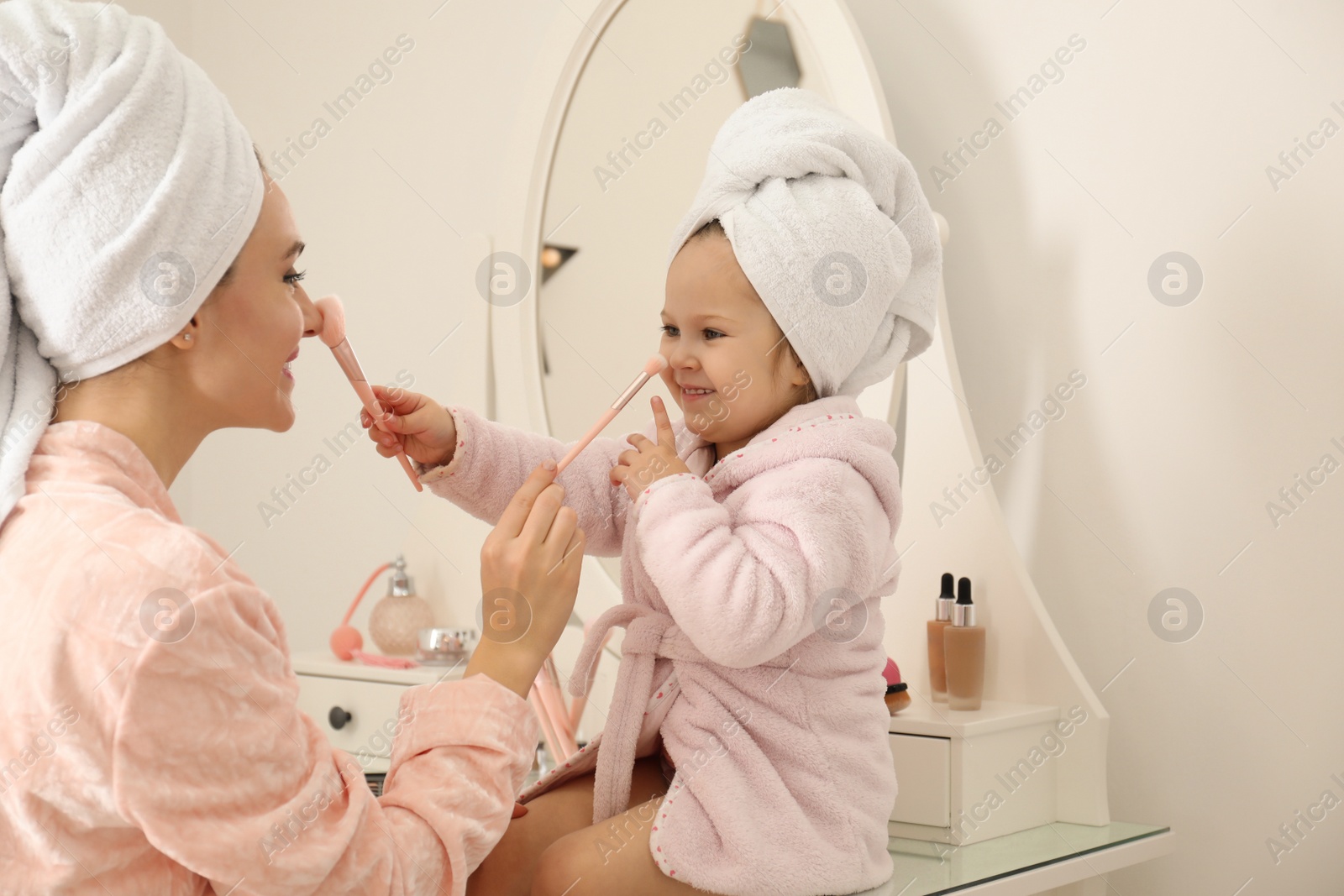 Photo of Young mother and little daughter doing makeup at dressing table