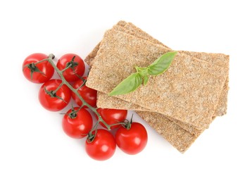 Photo of Crunchy rye crispbreads, fresh cherry tomatoes and basil on white background, top view