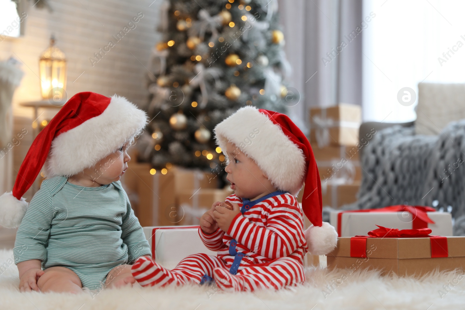 Image of Cute children in Santa hats on floor in room with Christmas tree