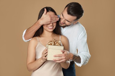 Photo of Man presenting gift to his girlfriend on beige background