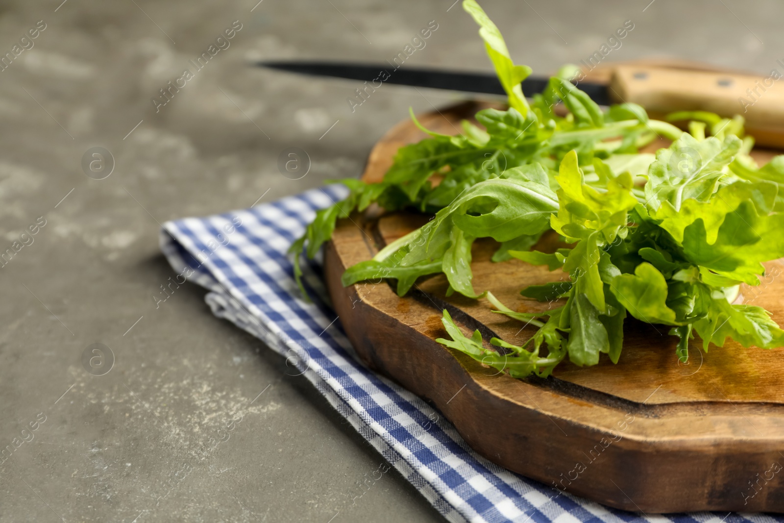 Photo of Fresh arugula and cutting board on grey table, closeup. Space for text