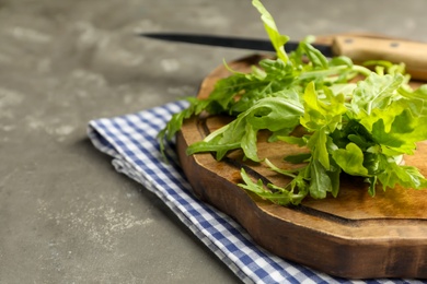 Photo of Fresh arugula and cutting board on grey table, closeup. Space for text