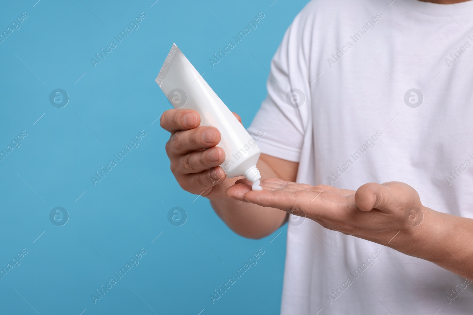 Photo of Man applying body cream onto his hand on light blue background, closeup. Space for text