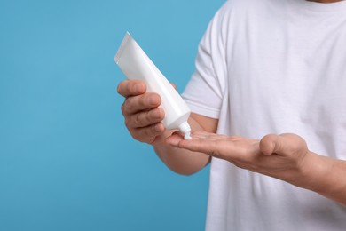 Man applying body cream onto his hand on light blue background, closeup. Space for text