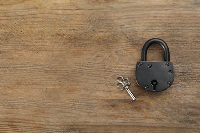 Vintage padlock with key on wooden table, flat lay. Space for text