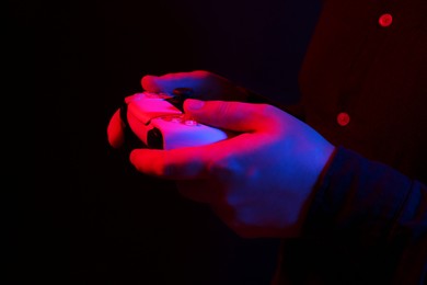 Man using wireless game controller on dark background in neon lights, closeup