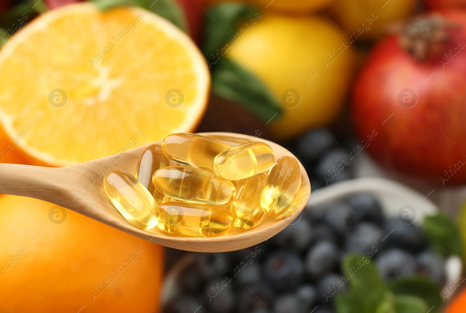 Photo of Vitamin pills in wooden spoon over fresh fruits, closeup. Space for text