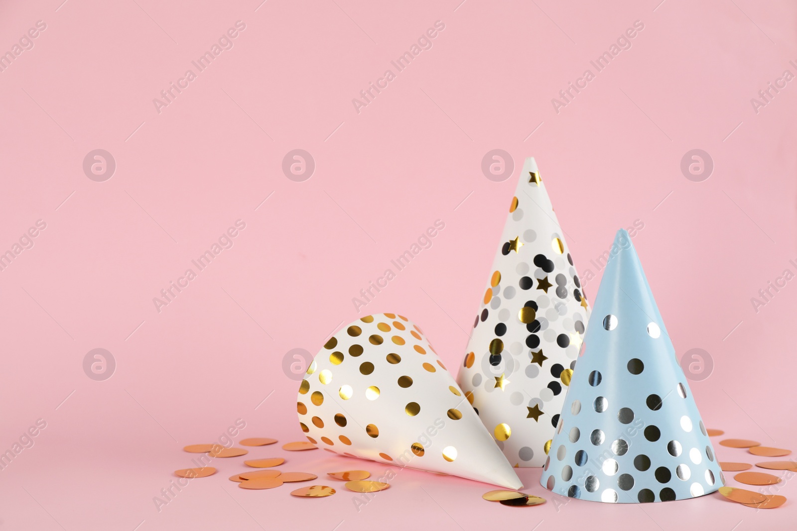 Photo of Bright party hats and confetti on pink background. Space for text