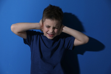 Photo of Scared little boy closing his ears near blue wall. Domestic violence concept