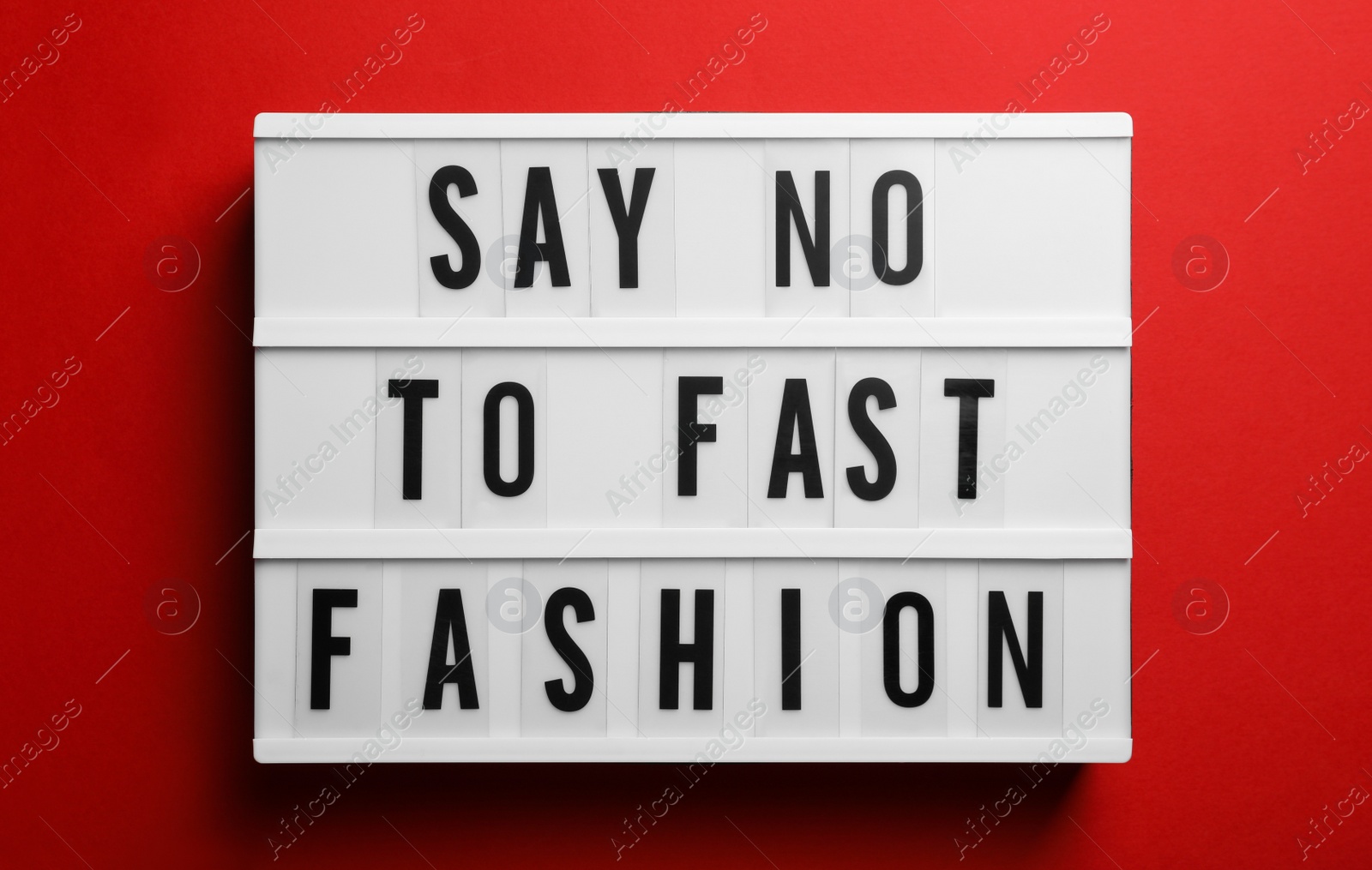 Photo of Lightbox with phrase SAY NO TO FAST FASHION on red background, top view