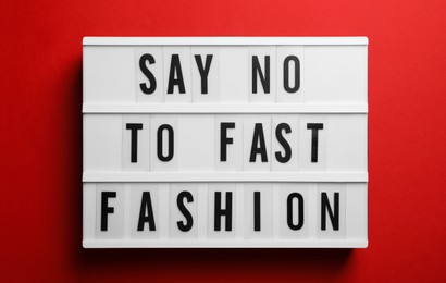 Photo of Lightbox with phrase SAY NO TO FAST FASHION on red background, top view