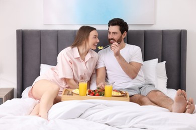 Photo of Healthy breakfast. Happy husband feeding his wife on bed at home