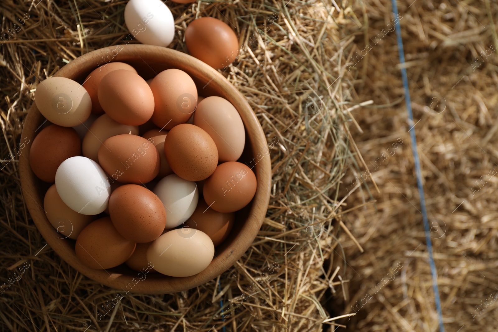 Photo of Fresh chicken eggs in bowl on dried straw bale, top view. Space for text