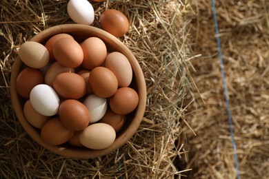 Photo of Fresh chicken eggs in bowl on dried straw bale, top view. Space for text