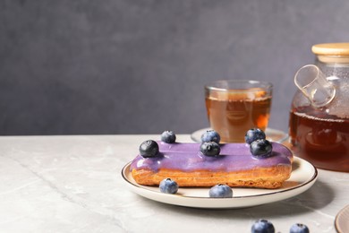 Tasty glazed eclair with blueberries on light table, closeup. Space for text