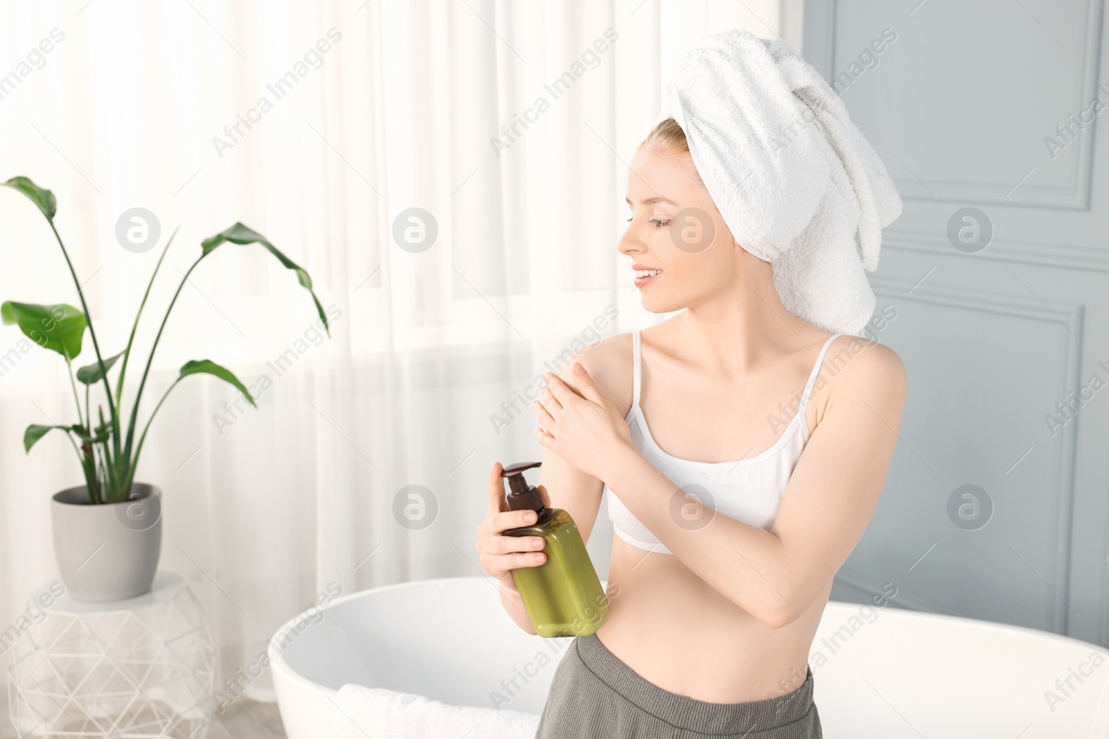 Photo of Beautiful young woman applying oil onto shoulder in bathroom