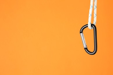 Photo of One metal carabiner hanging on rope against orange background. Space for text