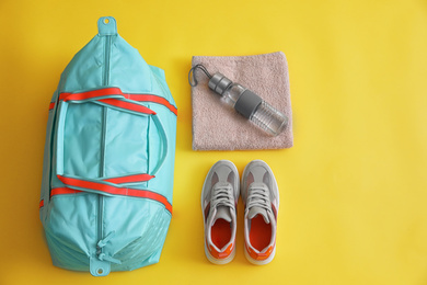 Gym bag and sports equipment on yellow background, flat lay