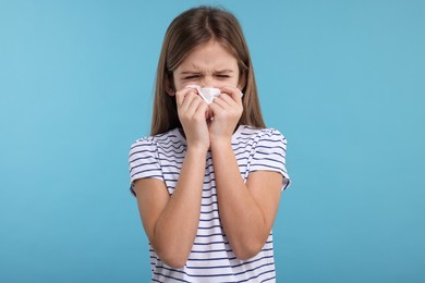 Photo of Sick girl with tissue coughing on light blue background