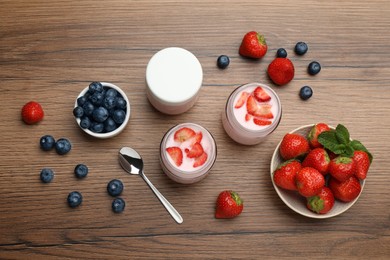 Photo of Jars of fresh yogurt, strawberry and blueberry on wooden table, flat lay